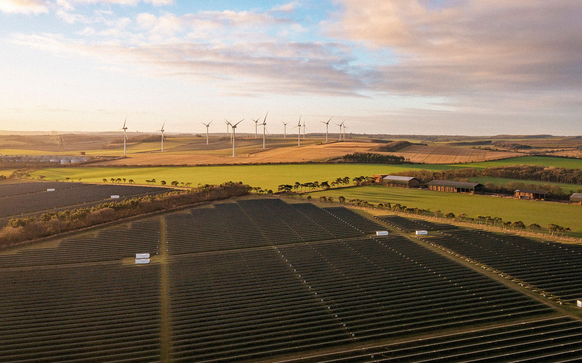 Solar panels and wind turbines in fields with the sunset in sky