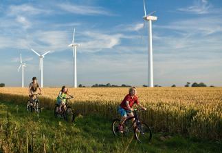 Children riding bikes through field with backdrop of wind turbines