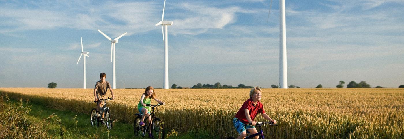 Children riding bikes through field with backdrop of wind turbines