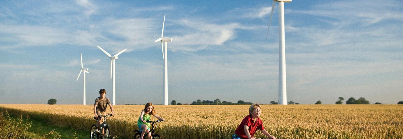 Children riding bikes through field with backdrop of wind turbines