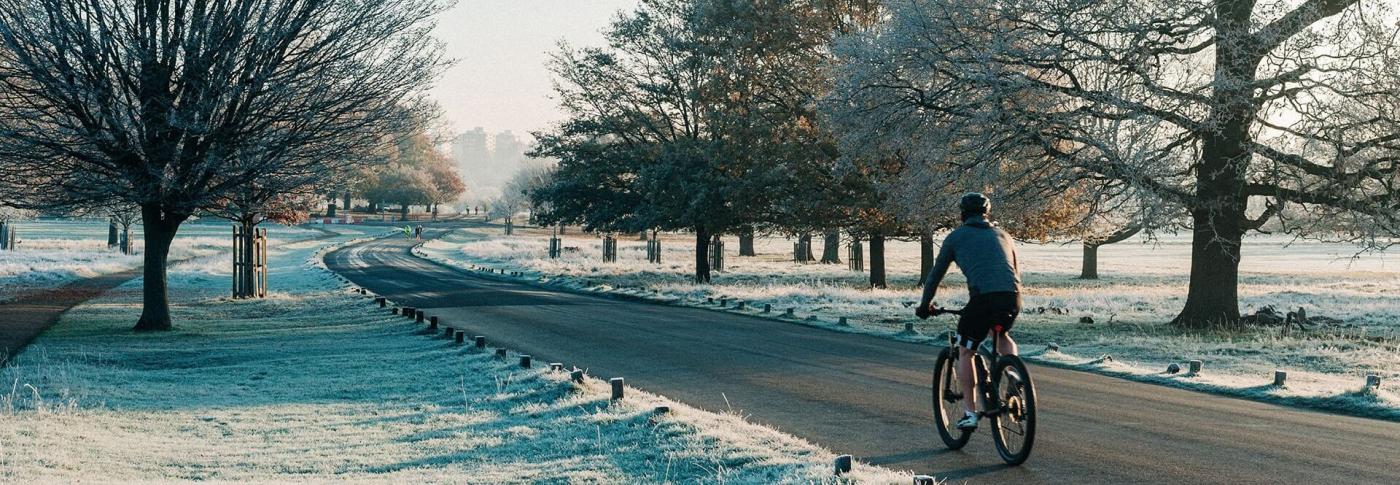Person cycling on a straight road with frost on the trees and ground