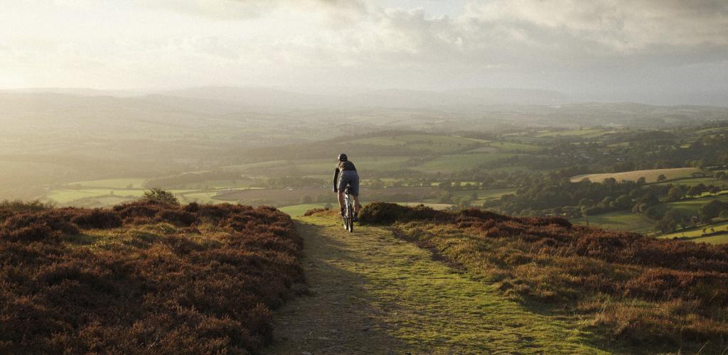 Cyclist about to ride down hill into sunset