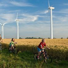 Children riding bikes through field with backdrop of wind turbines