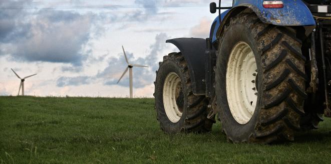 Big blue tractor and wind turbines in background