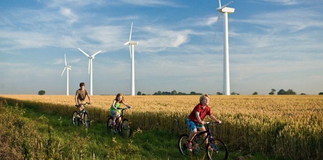 Children riding bikes through field with backdrop of wind turbines