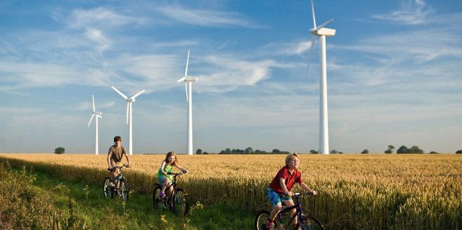 Children riding bikes through field with backdrop of wind turbines