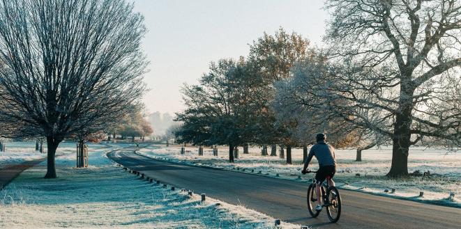 Person cycling on a straight road with frost on the trees and ground