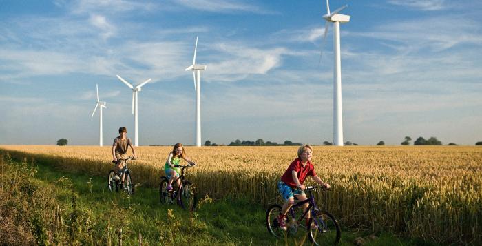 Children riding bikes through field with backdrop of wind turbines