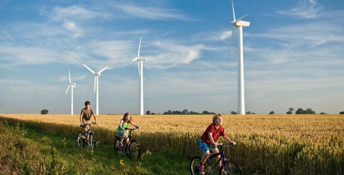 Children riding bikes through field with backdrop of wind turbines