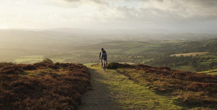 Cyclist about to ride down hill into sunset