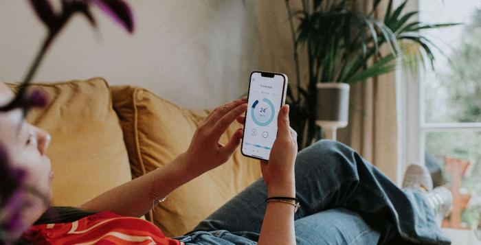 GettyImages-1389838100 person laid on sofa on their phone monitoring their heating